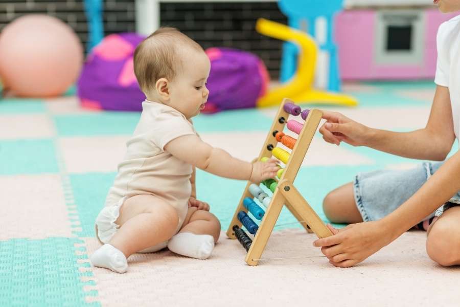 Un bébé apprend à manipuler un boulier avec l'aide d'un adulte pour son développement psychomoteur de bébé.