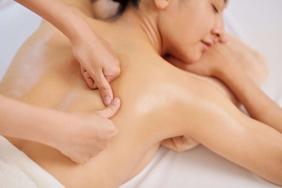 Gros plan d'une séance de masser le dos montrant les mains du masseur appuyant fermement avec les pouces sur la peau huilée d'une femme allongée sur le ventre.