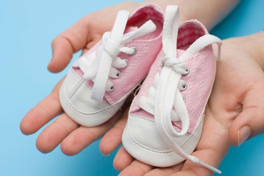 Des mains tenant des petites baskets roses pour illustrer l'achat des premières chaussures.