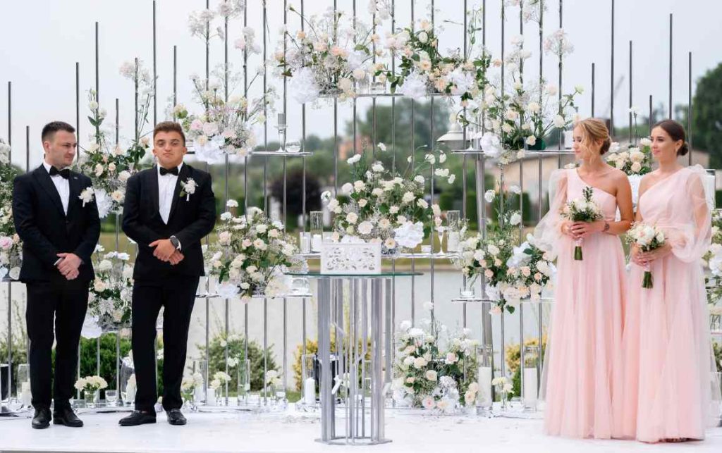 Deux témoins de mariage en robes roses et garçons d'honneur à l'autel illustrant quelles sont les missions de la témoin de mariage pendant la cérémonie.